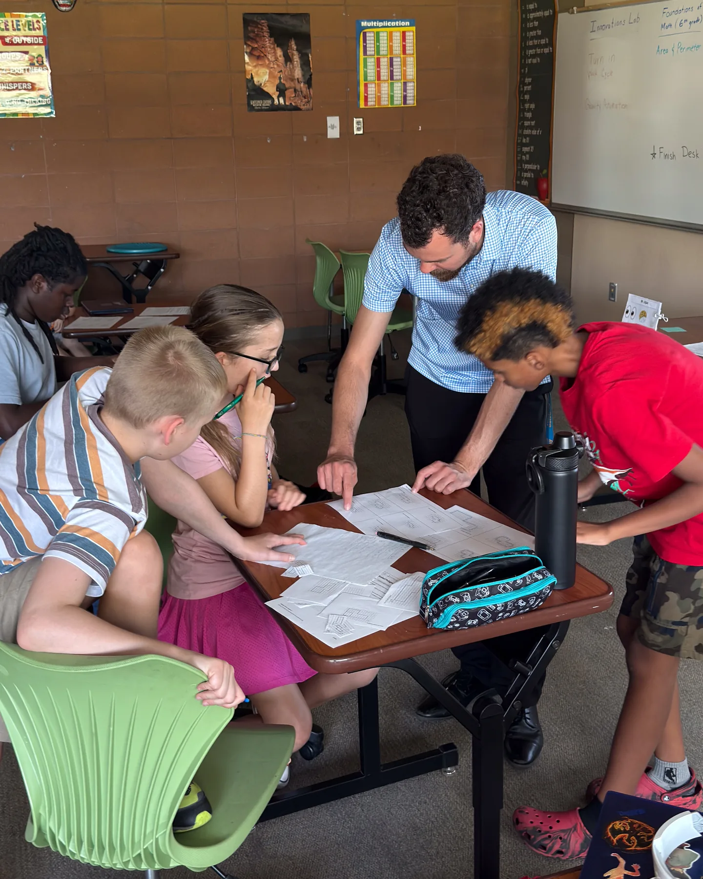 A teacher leaning in to help a group of Gateway students working through a project at a classroom desk