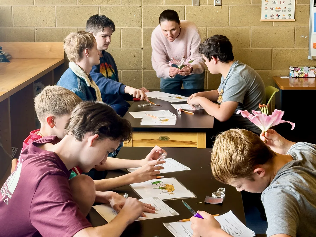 Gateway students dissecting flowers at a classroom table, a teacher helping at the far end