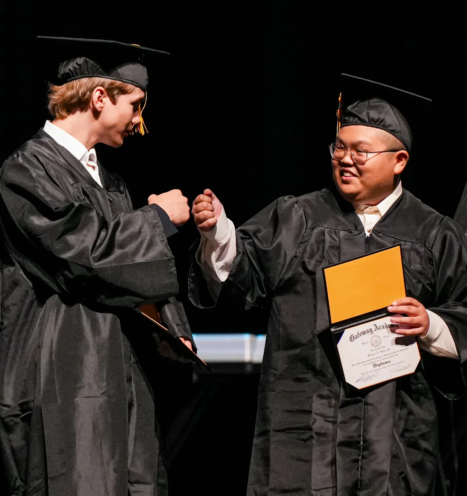 Two Gateway graduates bumping fists on stage at the 2026 commencement