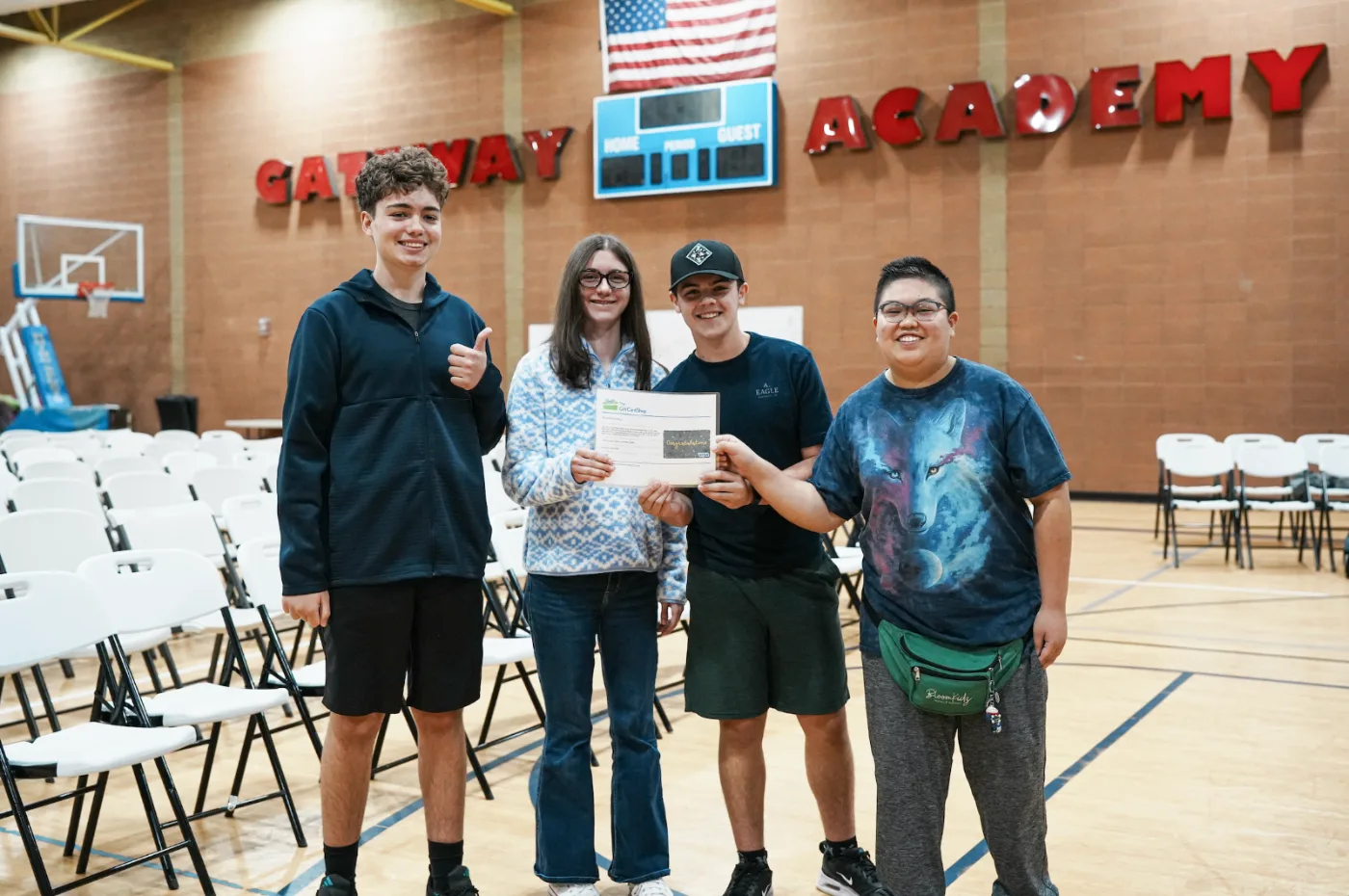 Four Gateway students in the gym holding a Quiz Bowl award, smiling